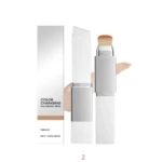 Base hidratante vegana con cambio de color, presentación en stick con aplicador de cerdas y muestra de tono natural. Incluye caja y envoltorio blanco.