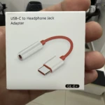 Adaptador USB-C a jack de 3.5 mm en caja blanca, con cable rojo y conectores plateados, modelo GL-E+.
