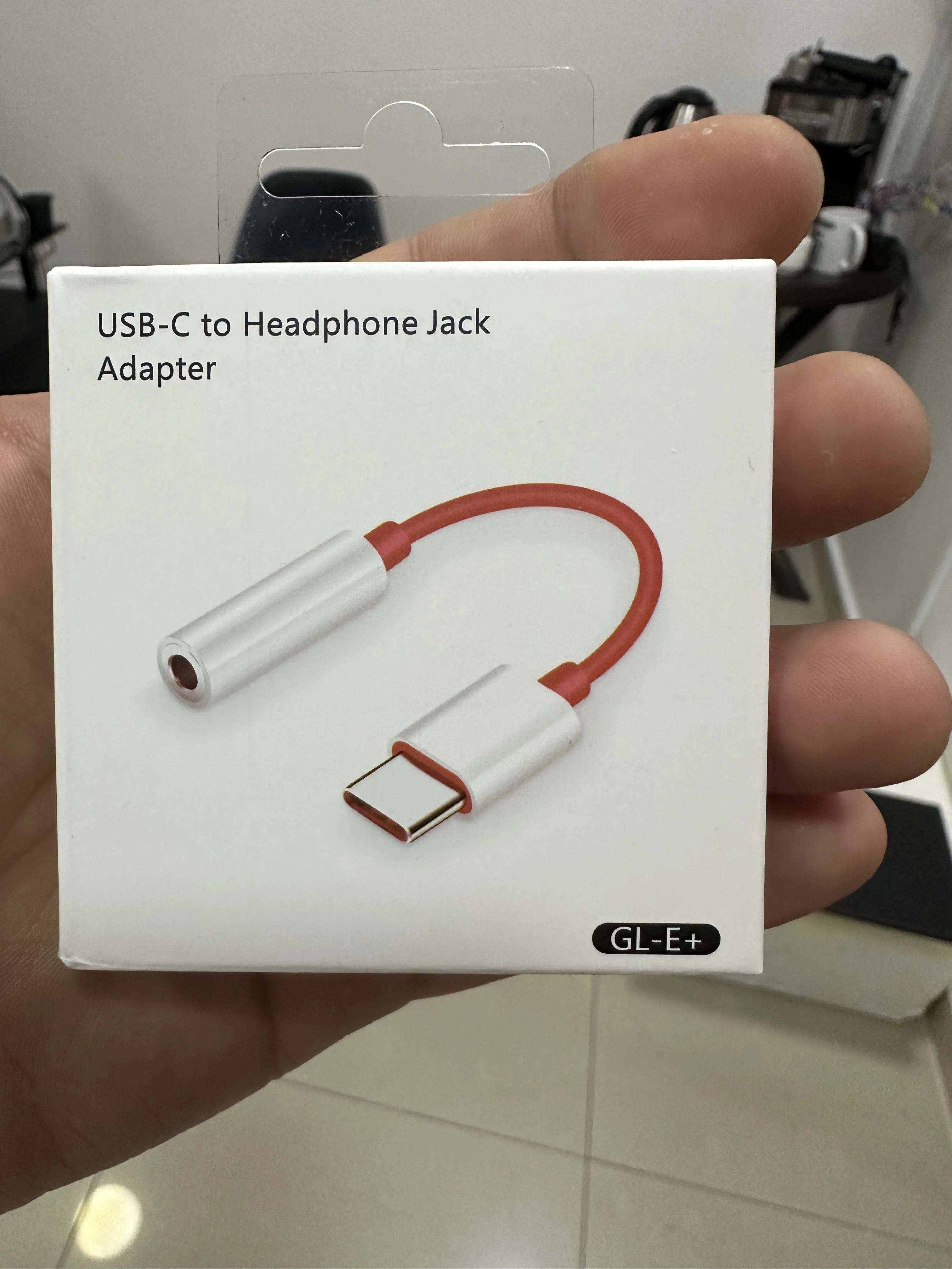 Adaptador USB-C a jack de 3.5 mm en caja blanca, con cable rojo y conectores plateados, modelo GL-E+.