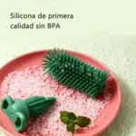Cepillo de silicona verde para limpiar biberones, con cerdas flexibles y mango ergonómico, sobre plato rosa con gránulos blancos y hojas de menta.