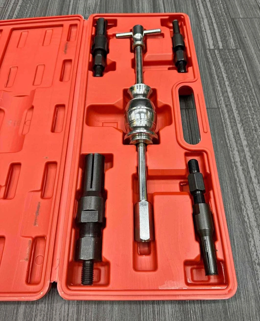 Extractor de rodamientos interno de 5 piezas en caja naranja con herramientas metálicas y accesorios negros dispuestos en compartimentos.