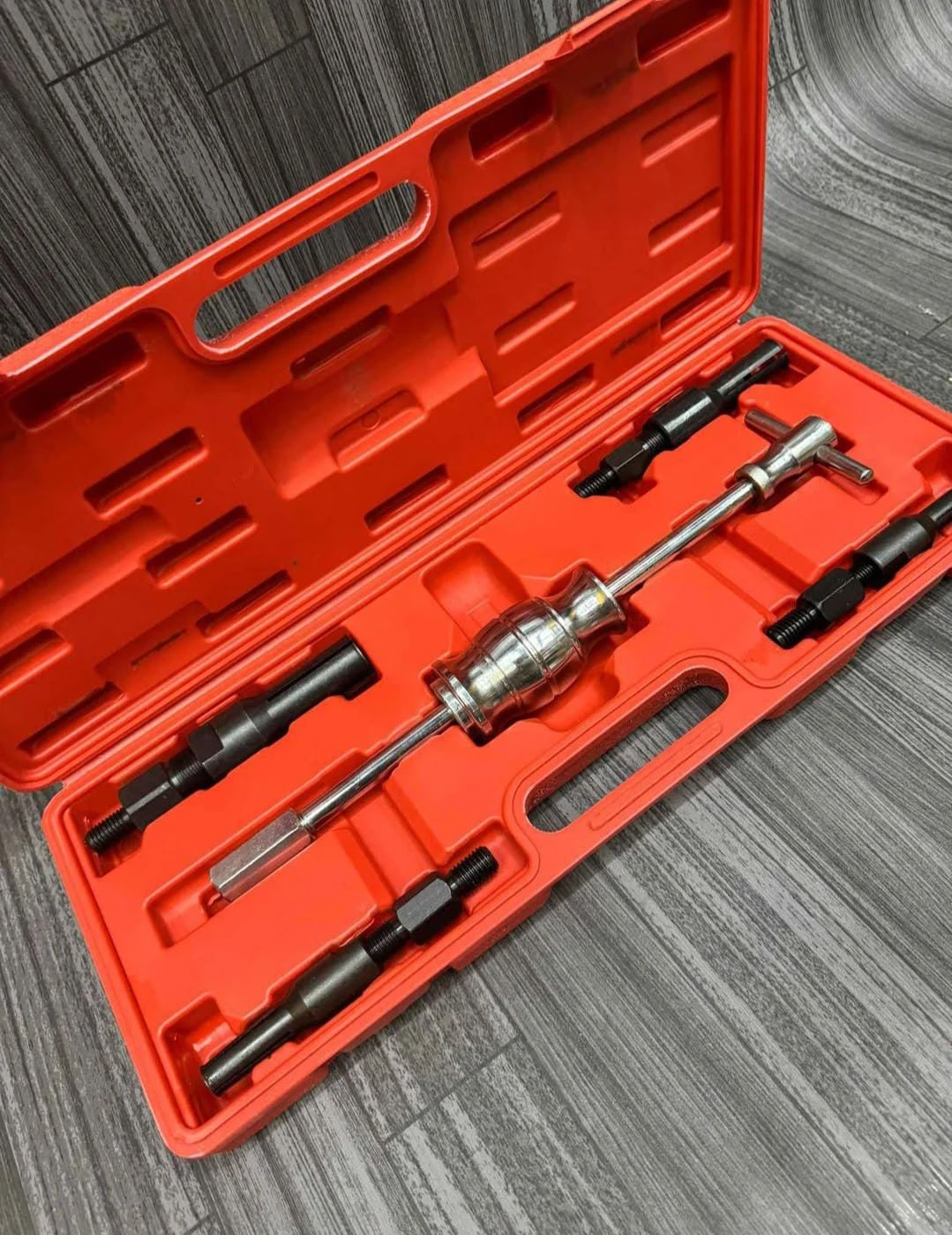Caja naranja abierta con extractor de rodamientos interno de 5 piezas, incluyendo herramienta central metálica y accesorios negros, sobre superficie gris texturizada.