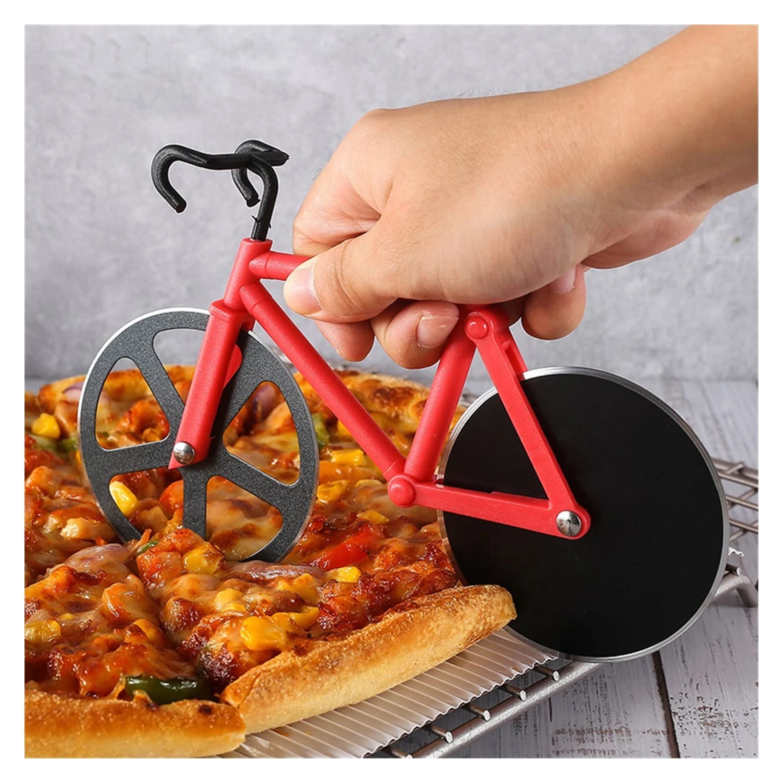 Rebanador de pizza en forma de bicicleta, con ruedas negras y cuadro rojo, siendo usado para cortar una pizza sobre rejilla metálica.