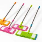Cuatro traperos de microfibra con varillas metálicas de 1 metro, en colores naranja, rosa, verde y azul, diseñados para limpiar esquinas y rincones difíciles.