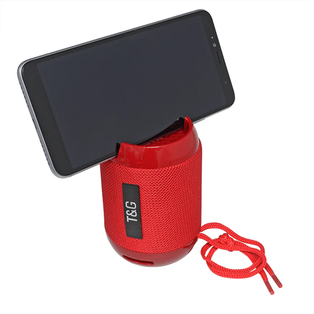 Bocina roja con soporte para celular, mostrando dispositivo negro insertado en su ranura superior y correa de transporte roja colgando lateralmente.