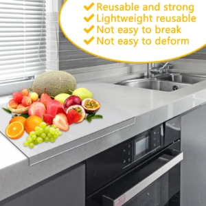 Tabla protector de mesa acrílica transparente sobre encimera de cocina, con frutas frescas encima; incluye texto promocional en español.