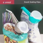 Tres pinzas para sellar bolsas de cocina en colores blanco, turquesa y gris, aplicadas sobre paquetes de snacks y arroz, con tapas plásticas y mangos ergonómicos.