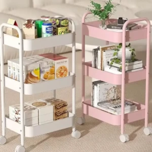 Carrito organizador de tres niveles en metal, disponible en blanco y rosa, con ruedas para movilidad y estantes para libros, cajas y plantas.