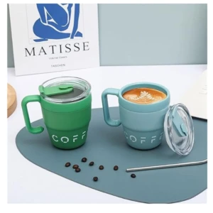 Taza térmica de acero inoxidable en verde y azul claro, con tapa antideslizante y diseño ergonómico. Incluye café con arte latte y café en grano sobre superficie azul.