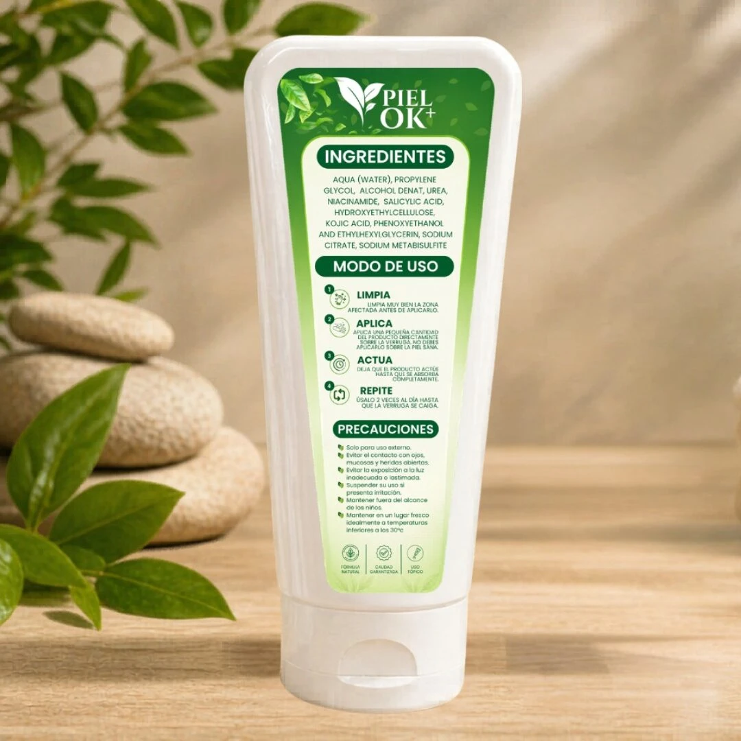 Tubo blanco de Piel Ok con etiqueta verde, mostrando ingredientes y modo de uso, sobre madera con hojas y piedras decorativas al fondo.