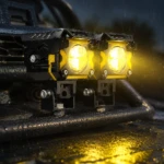 Faros LED Moto-Carro Jry-16 de 30W, color negro, instalados en barra frontal de vehículo, emitiendo luz amarilla intensa bajo lluvia.