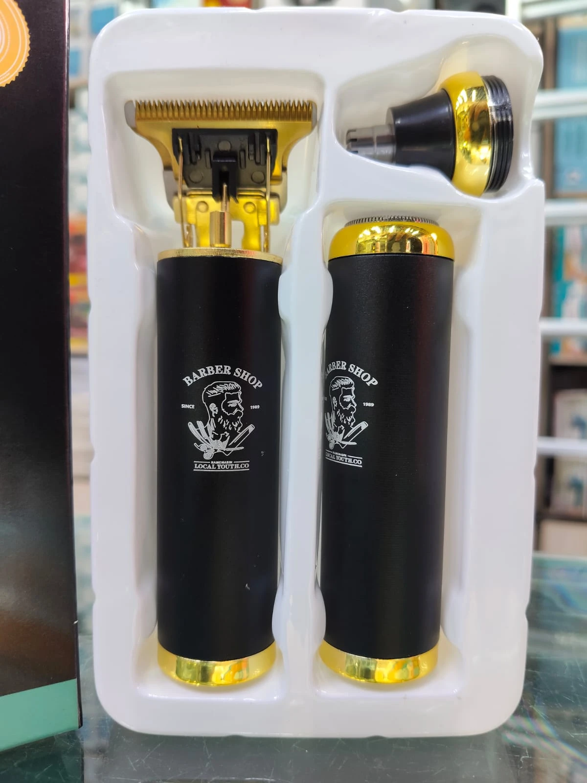 Máquina eléctrica híbrida negra con detalles dorados, incluye cabezal de corte y accesorio nasal, presentada en su empaque original.
