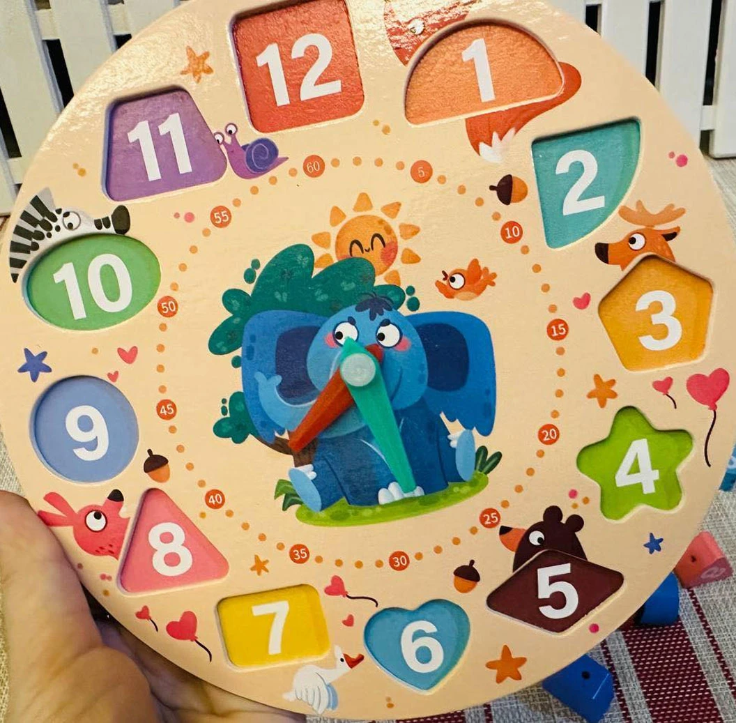 Reloj educativo de madera con bloques numerados del 1 al 12, diseño circular con elefante azul central y animales alrededor, ideal para motricidad fina.
