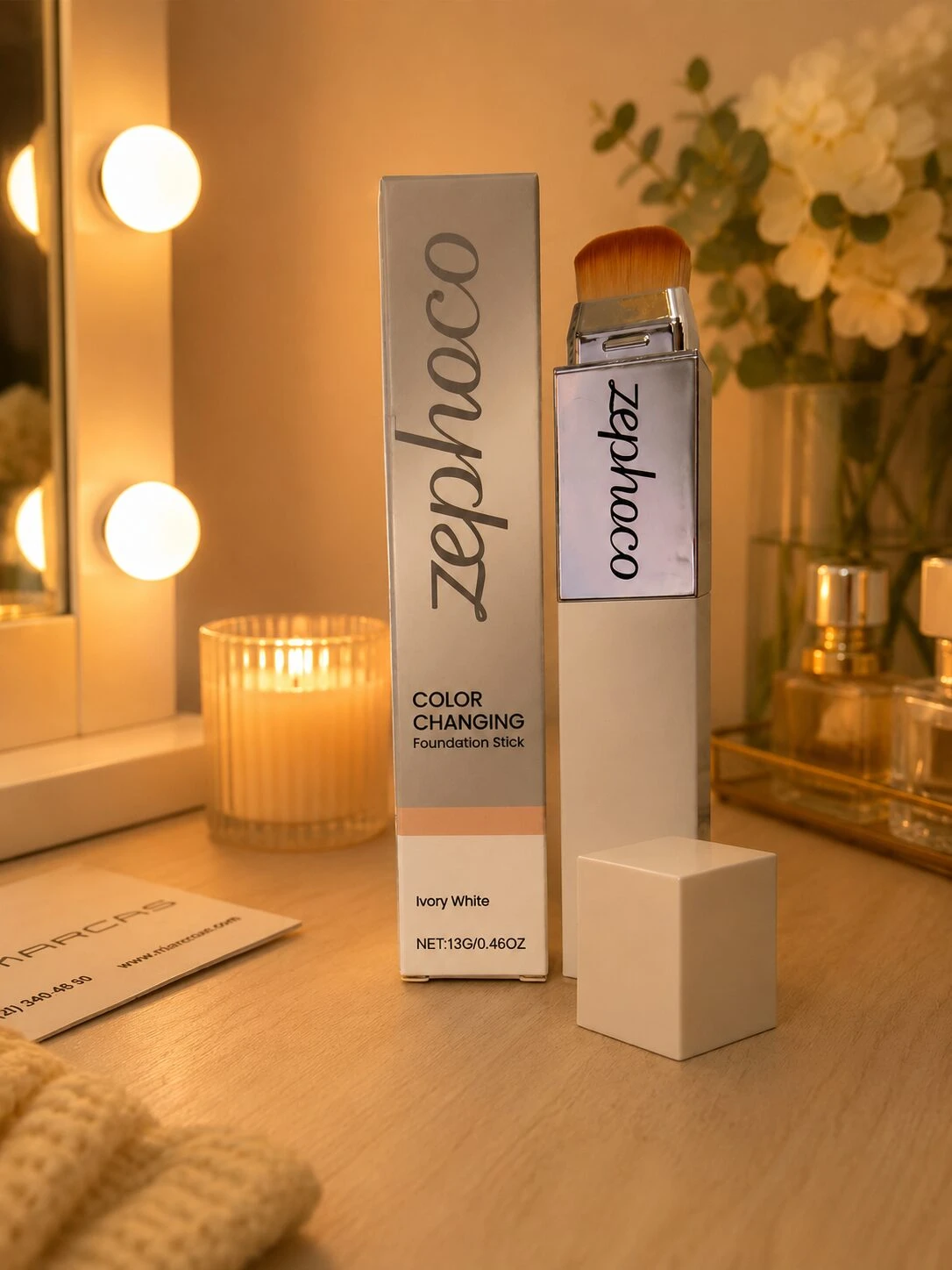 Base de maquillaje en barra Zephco color ivory white, con cepillo incluido, sobre mesa de tocador con velas y flores.
