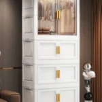 Organizador de plástico blanco con puertas transparentes y tiradores dorados, mostrando ropa colgada en el interior.