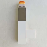 Base hidratante vegana con cambio de color, presentación rectangular en blanco y plateado, brocha naranja visible en la parte superior.