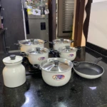 Batería de cocina Alfusa White con jarra y sartén antiadherente, sobre encimera negra.