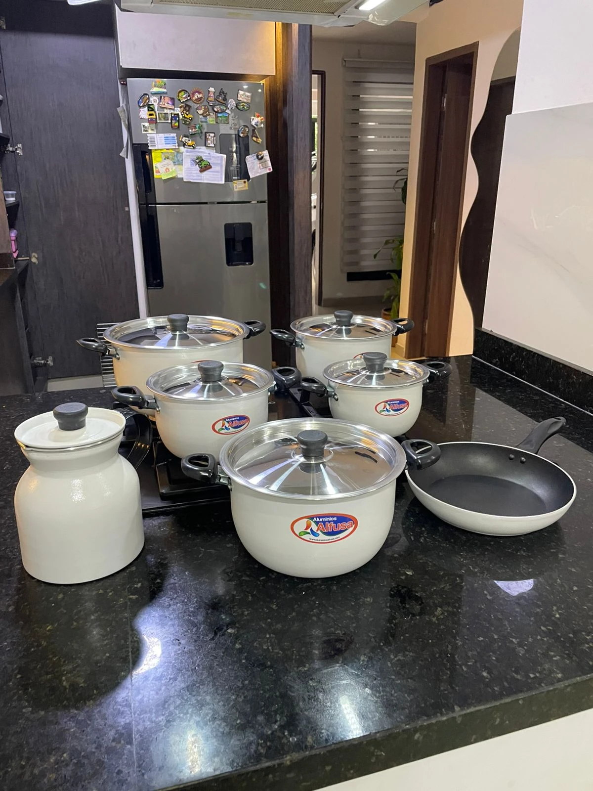 Batería de cocina Alfusa White con jarra y sartén antiadherente, sobre encimera negra.