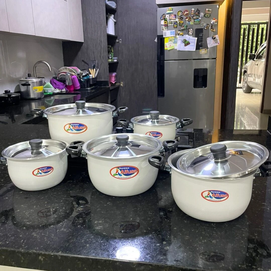 Set de ollas blancas Alfusa con tapa de vidrio, dispuestas sobre encimera oscura en cocina moderna.