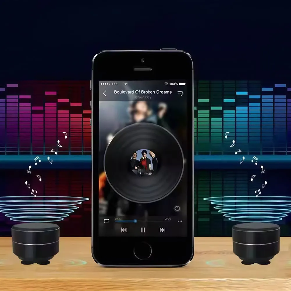 Altavoz portátil negro con pantalla de smartphone mostrando reproducción musical, acompañado de dos altavoces pequeños sobre superficie de madera.