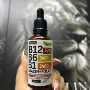 Frasco de vidrio ámbar con gotero de 50 ml y etiqueta blanca de Nusava B12, B6 y B1 con niacina y folate sabor a frambuesa.