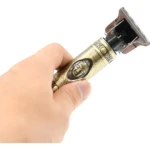 Máquina de afeitar eléctrica WS-T99 con diseño ornamental dorado y relieve de Buda, sostenida en mano para mostrar su acabado metálico y cabezal de corte.