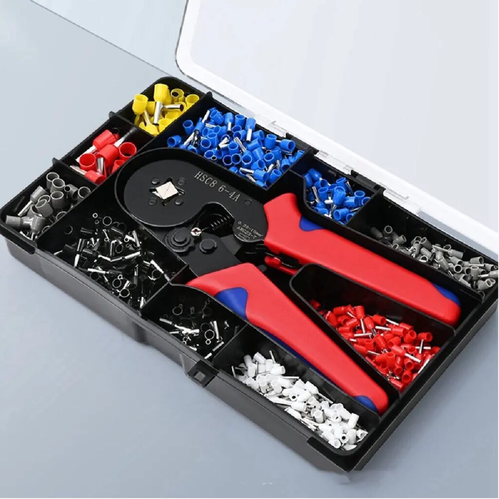 Pinza prensadora de terminales tubulares con trinquete, en caja organizadora negra con compartimentos para conectores amarillos, rojos, azules y blancos, sobre fondo gris claro.