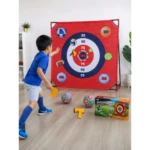 Niño en acción lanzando pelotas de fútbol, baloncesto y voleibol hacia diana roja con anillos numerados de 25 a 100, junto a caja del juego y accesorios amarillos sobre piso de madera.