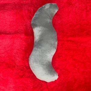 Almohada ergonómica tipo gusano en color gris claro sobre fondo rojo, diseñada para dormir de lado y mejorar la postura.