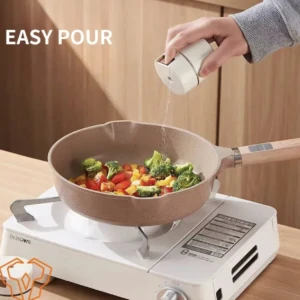 Condimentero blanco con visor y botón de presión, vertiendo especias sobre verduras en sartén sobre estufa portátil.