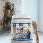 Contenedor de impermeabilizante Aguacero Gris 7A galón, con etiqueta visible y pincel de cerdas naturales al lado, sobre fondo blanco con pared afectada por humedad en el fondo.