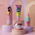 Kit de cuidado de la piel con cuatro productos: spray dorado, crema en tubo, jarra rosa y spray azul, sobre pedestales pastel frente a fondo dividido en tonos rosa y beige.