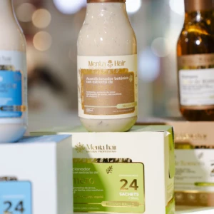 Acondicionador botánico de Mentahair en frasco blanco con tapa dorada, sobre caja verde que indica 24 sachets; fondo con otros productos y luces difusas.