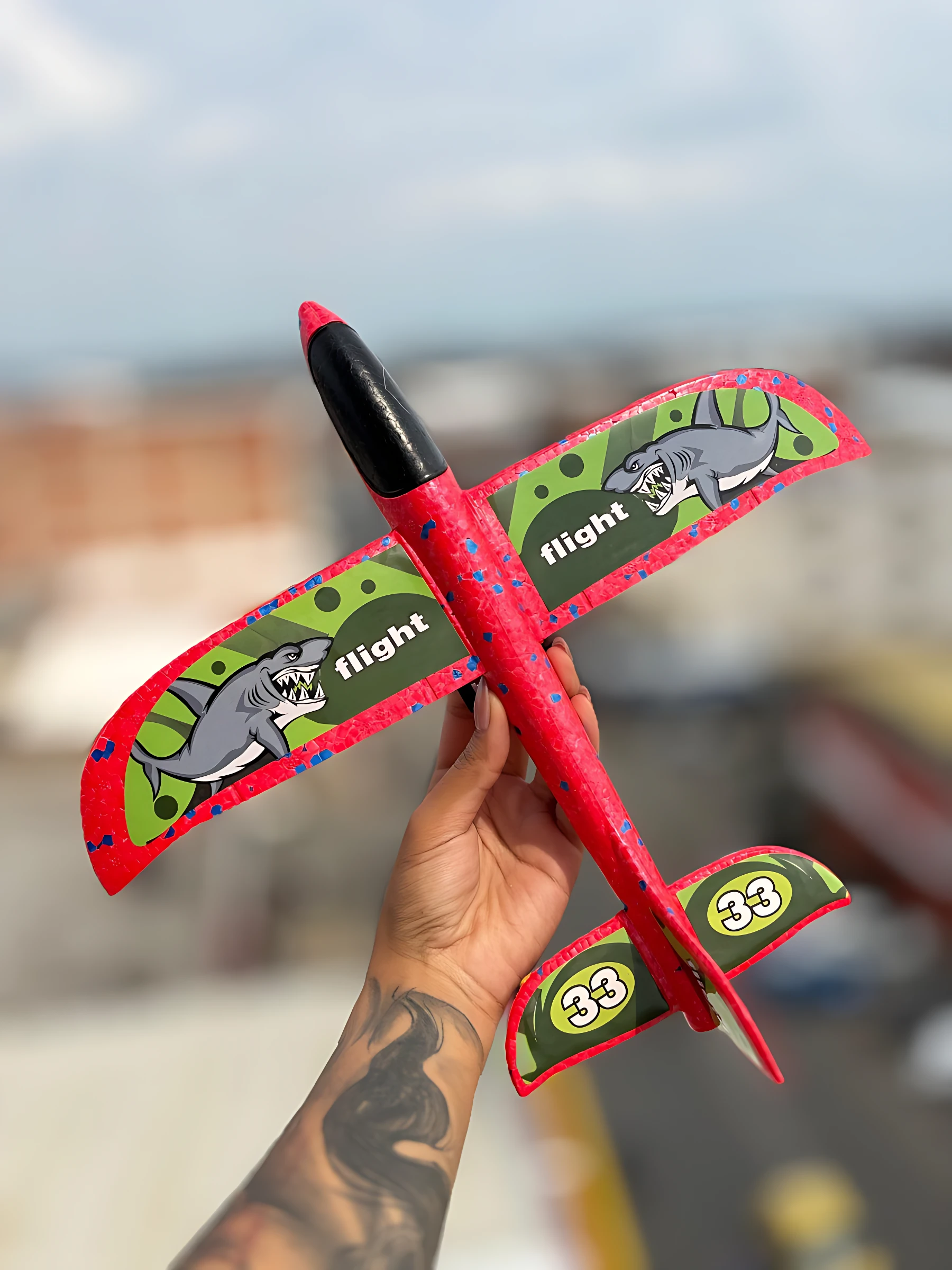 Avión lanzador T800A rojo con estampado de tiburones y números 33 en alas y cola, sostenido en mano sobre fondo urbano desenfocado.