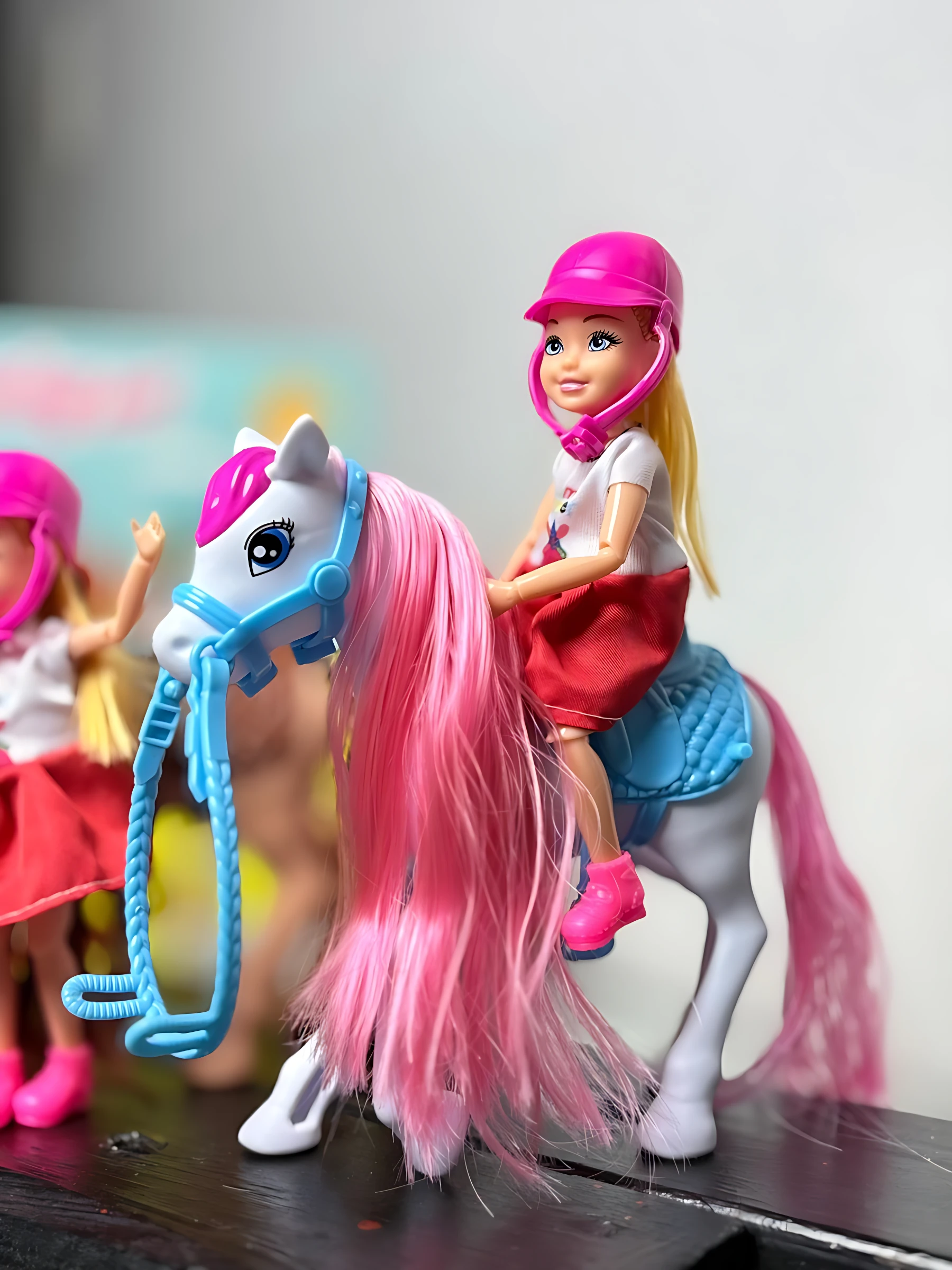 Barbie niña caballista con casco rosa montando caballo de peluche blanco y rosa, con brida azul y silla azul, sobre superficie oscura.