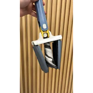 Barredora manual de empuje con cepillo giratorio en azul y amarillo, mostrando mecanismo de apertura y cepillo enrollado, sobre fondo de paneles verticales madera.