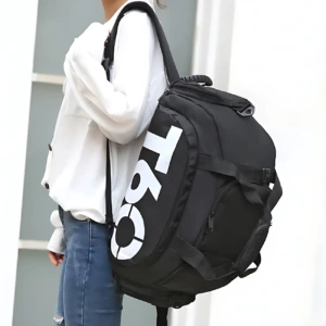 Bolso deportivo negro con diseño T60 en blanco, usado como mochila por persona con sudadera blanca y jeans. Incluye compartimento lateral para calzado.