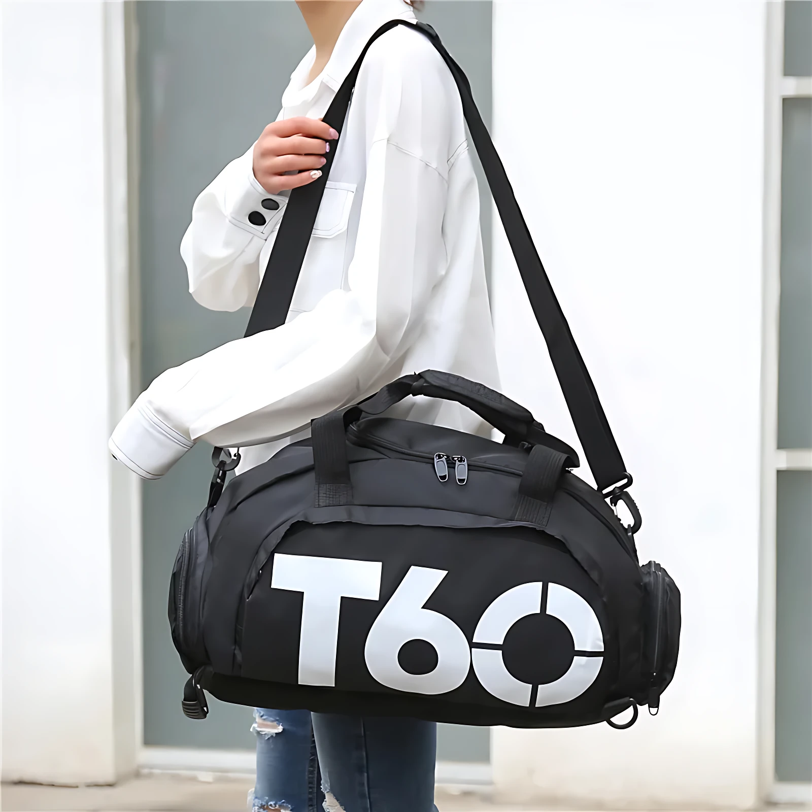 Bolso deportivo negro con logo T60 en blanco, asa superior y correa ajustable, usado por mujer con ropa casual.