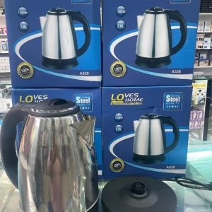 Tetera eléctrica Scarlett acero inoxidable 2L con base desmontable, mostrada junto a sus cajas de venta en estantería.