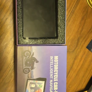Caja abierta de pantalla táctil para CarPlay en moto, color negro, con soporte de espuma y caja exterior morada que muestra de navegación y control de música.