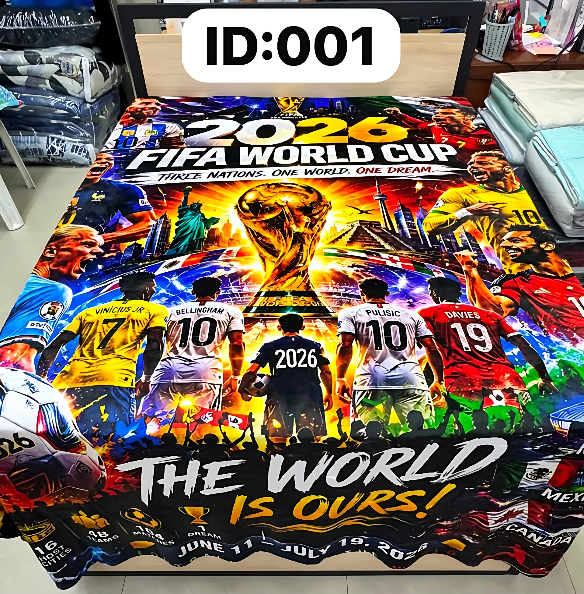 Cobija digitalizada con diseño de Copa Mundial FIFA 2026, mostrando jugadores y trofeo en colores vibrantes sobre fondo oscuro, con texto "THE WORLD IS OURS" en la parte inferior.