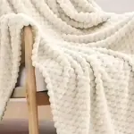 Cobija de punto grueso color crema sobre silla de madera, textura suave y acogedora.