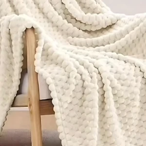 Cobija de punto grueso color crema sobre silla de madera, textura suave y acogedora.