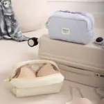 Dos cosméticas acolchadas en tonos pastel, una azul claro y otra crema, mostrando su interior con sujetador de color nude. Ambas reposan sobre una maleta beige.