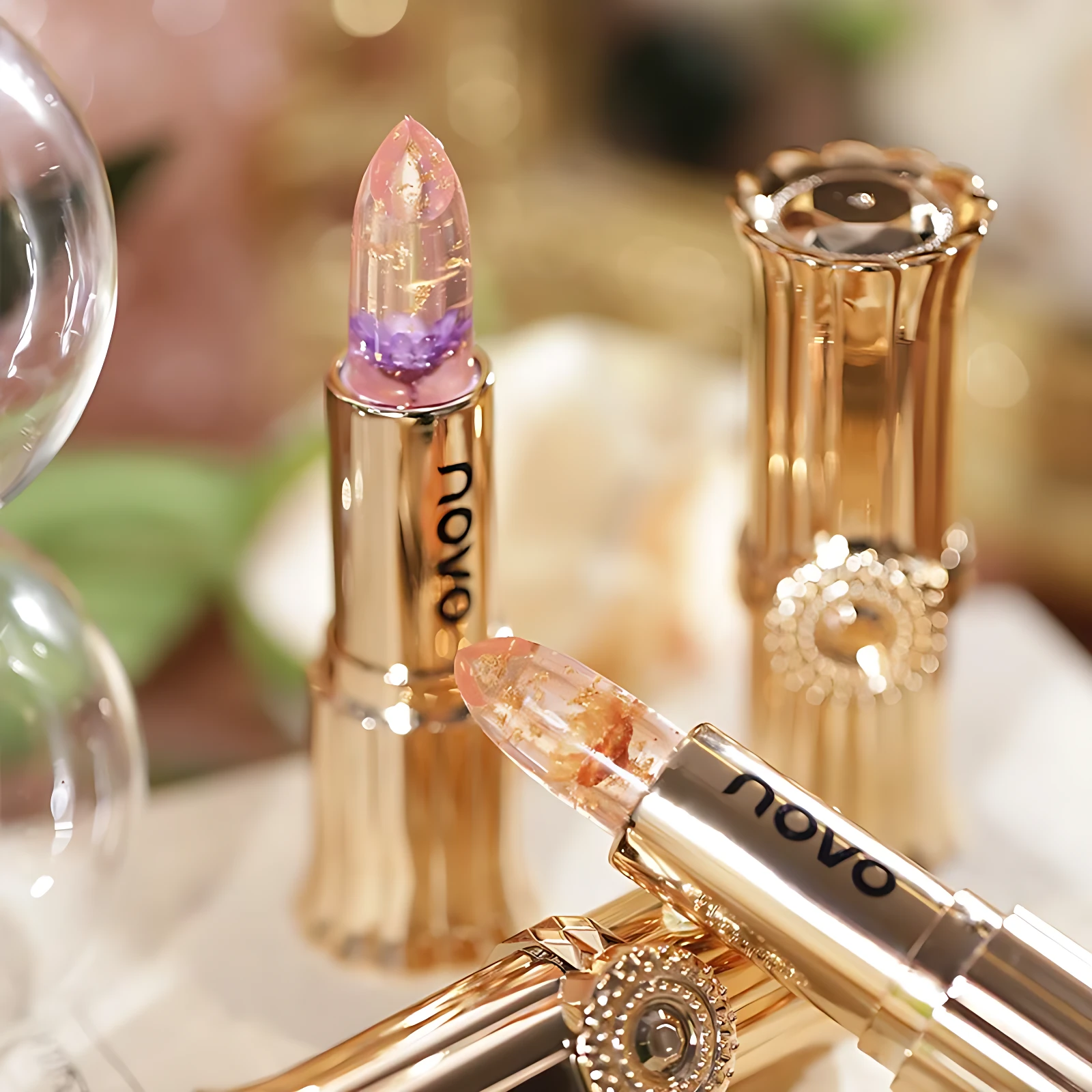 Labial en gel transparente con partículas brillantes, envase dorado y tapa removible, mostrando textura cristalina y acabado reflectante.
