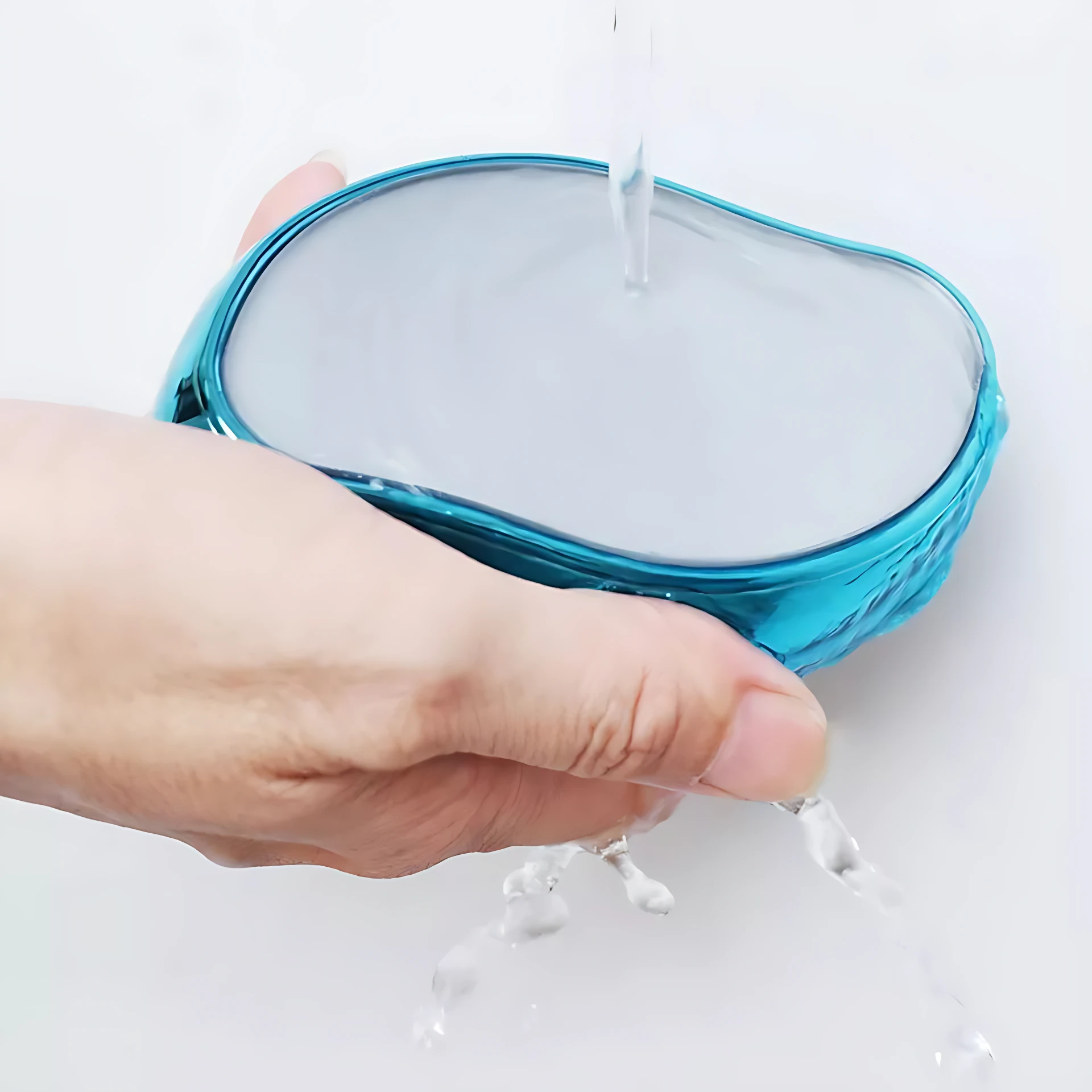 Depilador de cristal nano azul metálico, con superficie lisa y bordes redondeados, siendo enjuagado bajo chorro de agua mientras una mano lo sostiene.
