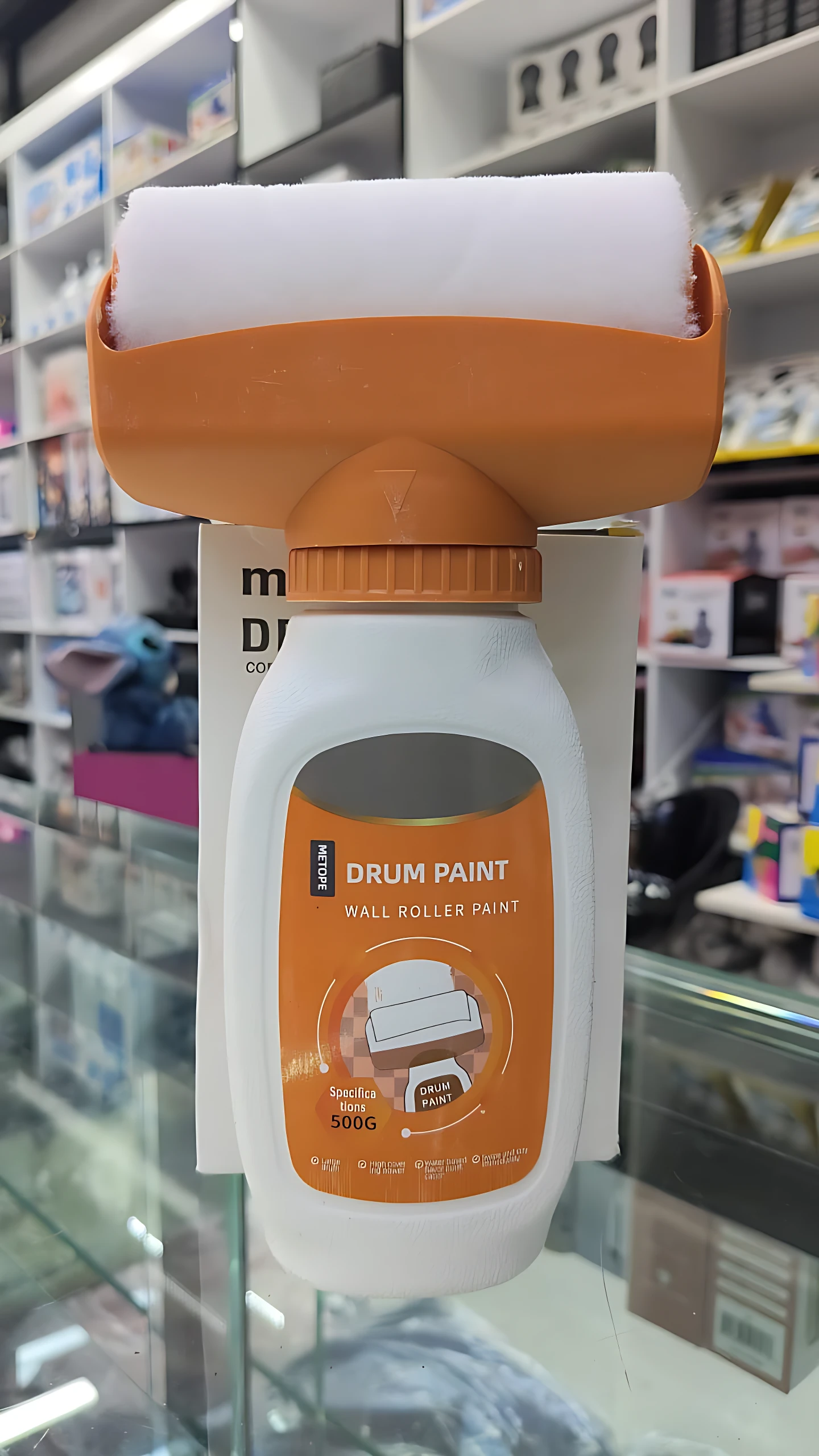 Pintura portátil Drum Paint con rodillo integrado, envase blanco y naranja de 500 g, ideal para retoques rápidos en paredes.