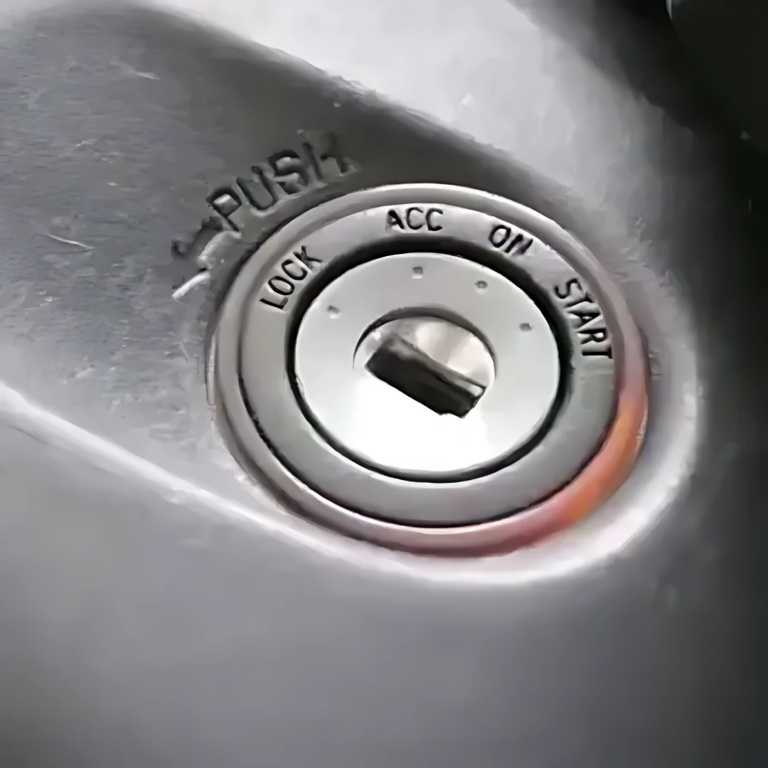 Cilindro de encendido de vehículo con llave en posición START, rodeado por anillo metálico con marcas LOCK, ACC, ON, START y botón PUSH superior.