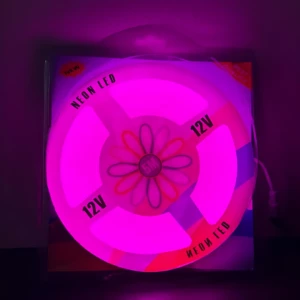 Tira LED rosada en empaque circular con luz encendida, adaptador 12V visible y diseño floral central.