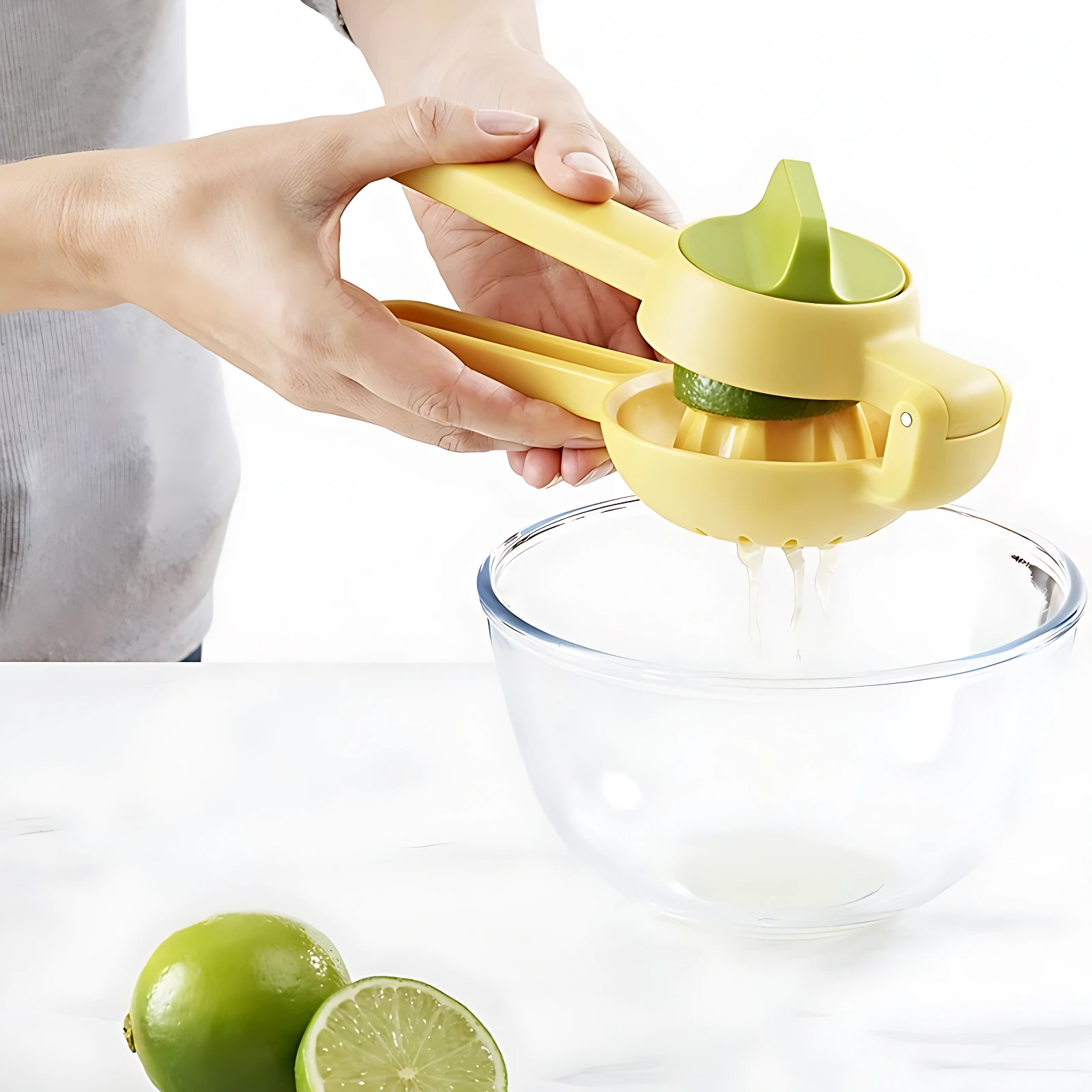 Exprimidor manual amarillo con mango verde, en uso sobre tazón transparente, exprimiendo lima. Incluye dos limas frescas en primer plano.